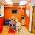Cheerful and clean, orange pediatric dental treatment room and chair in Florissant MO
